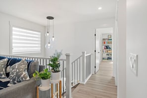 A modern living room with a sofa, a potted plant, and a staircase leading to a bookshelf. - Creekstone Retreat - South West Calgary - A Cozy Home for a Peaceful stay (Calgary)
