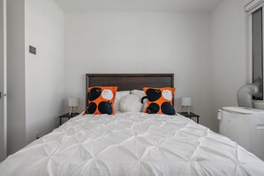 A hotel room with a white bed, two nightstands, a white lamp, a heater, and a window. - Creekstone Retreat - South West Calgary - A Cozy Home for a Peaceful stay (Calgary)