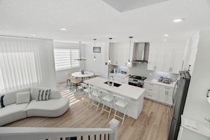 A modern kitchen with white cabinetry, a central island, and a dining area with a round table and chairs. - Creekstone Retreat - South West Calgary - A Cozy Home for a Peaceful stay (Calgary)