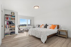 Ein Schlafzimmer mit einem großen Bett, einem Bücherregal, einem Schreibtisch und einem Fenster mit Blick.