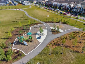 Eine Luftaufnahme einer Wohngegend mit einem Park, der Spielgeräte, einen gewundenen Weg und eine kleine Brücke zeigt.
