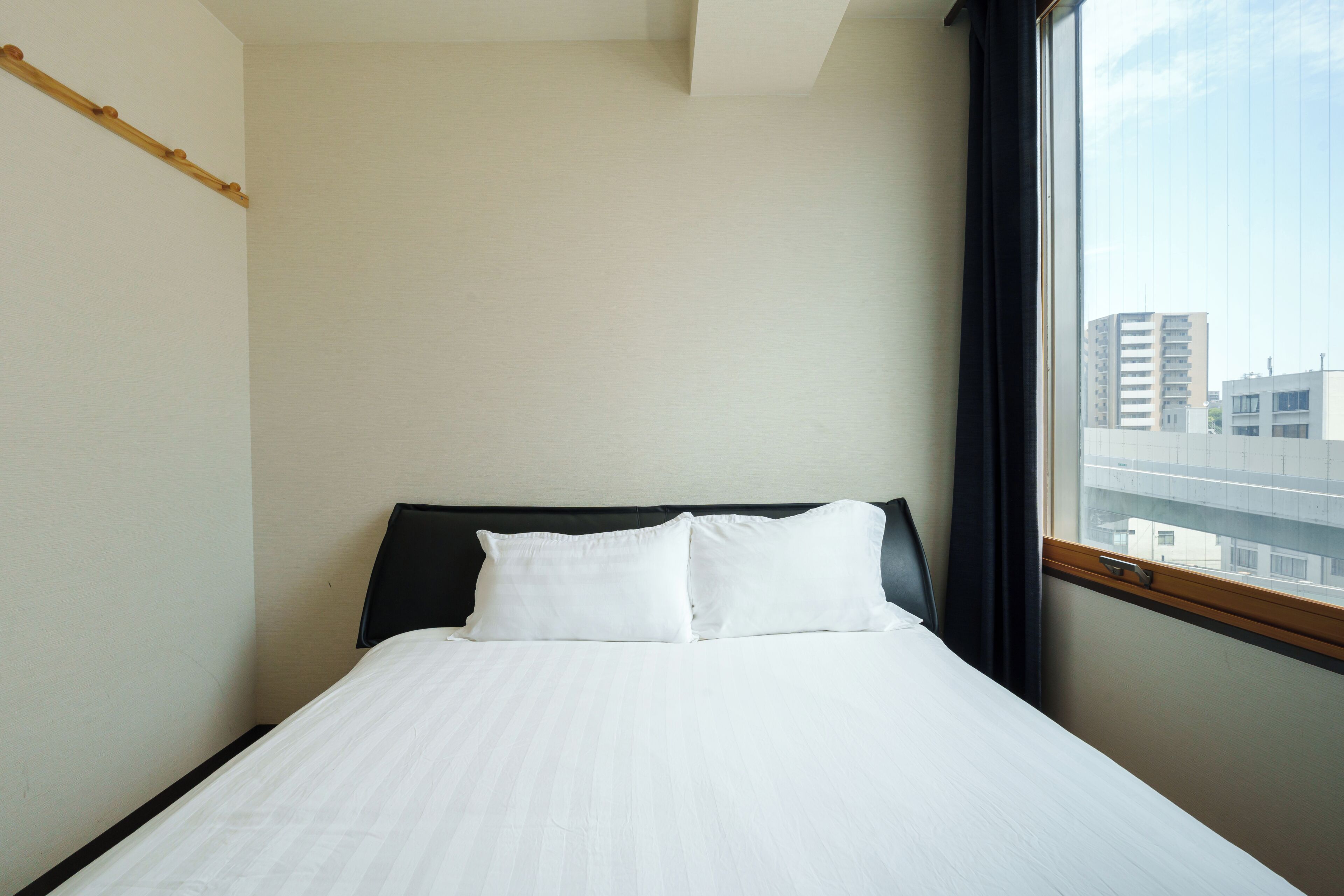 A hotel room with a bed, a window with a view of buildings, and a wooden headboard.