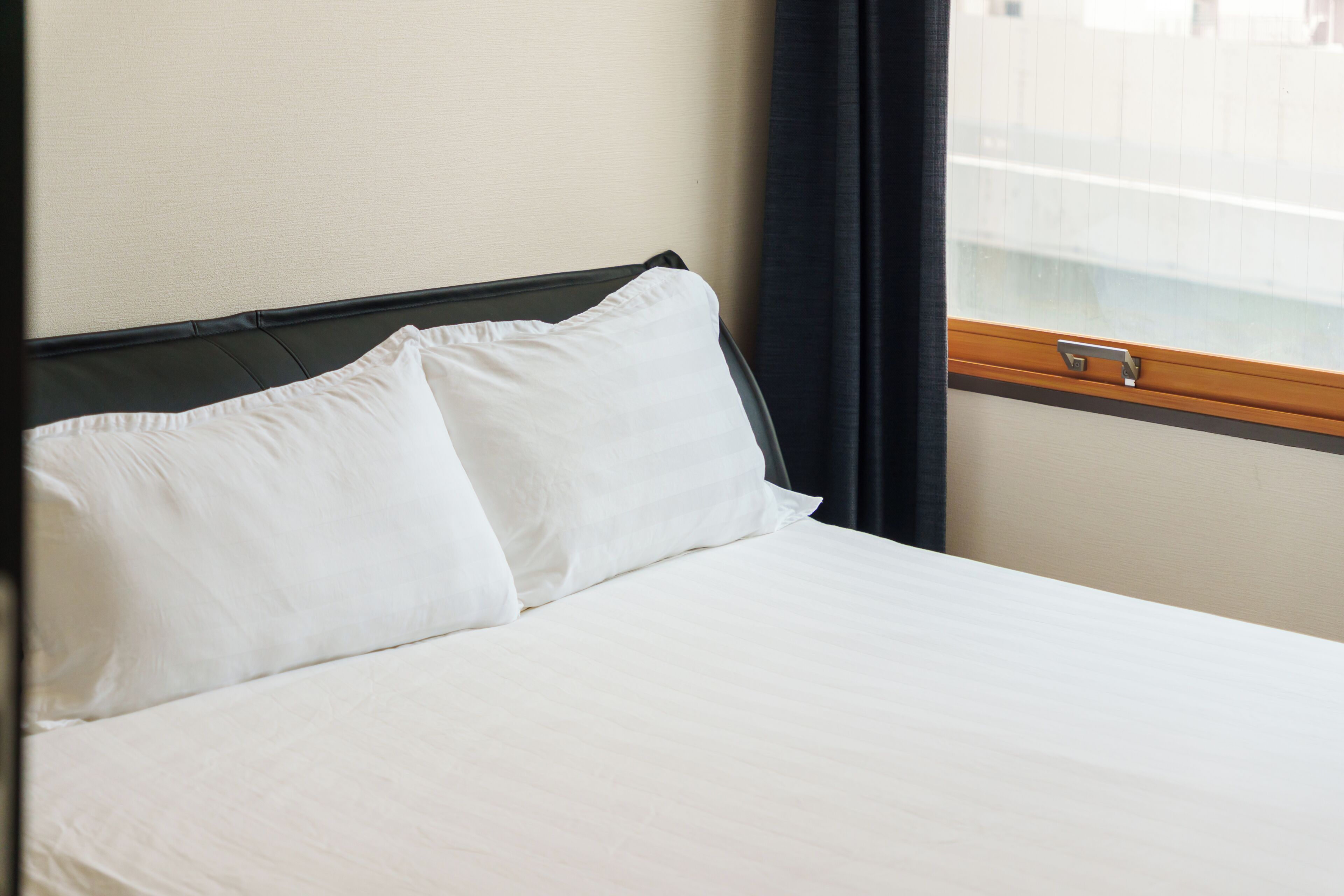 Een hotelkamer met een bed, een raam met gordijnen en een houten hoofdeinde.