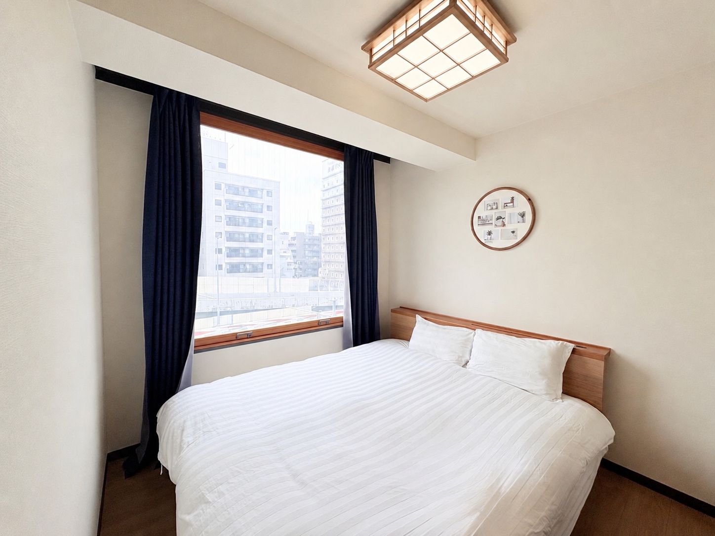 A hotel room with a bed, a window with curtains, a wall-mounted picture, and a ceiling light fixture.