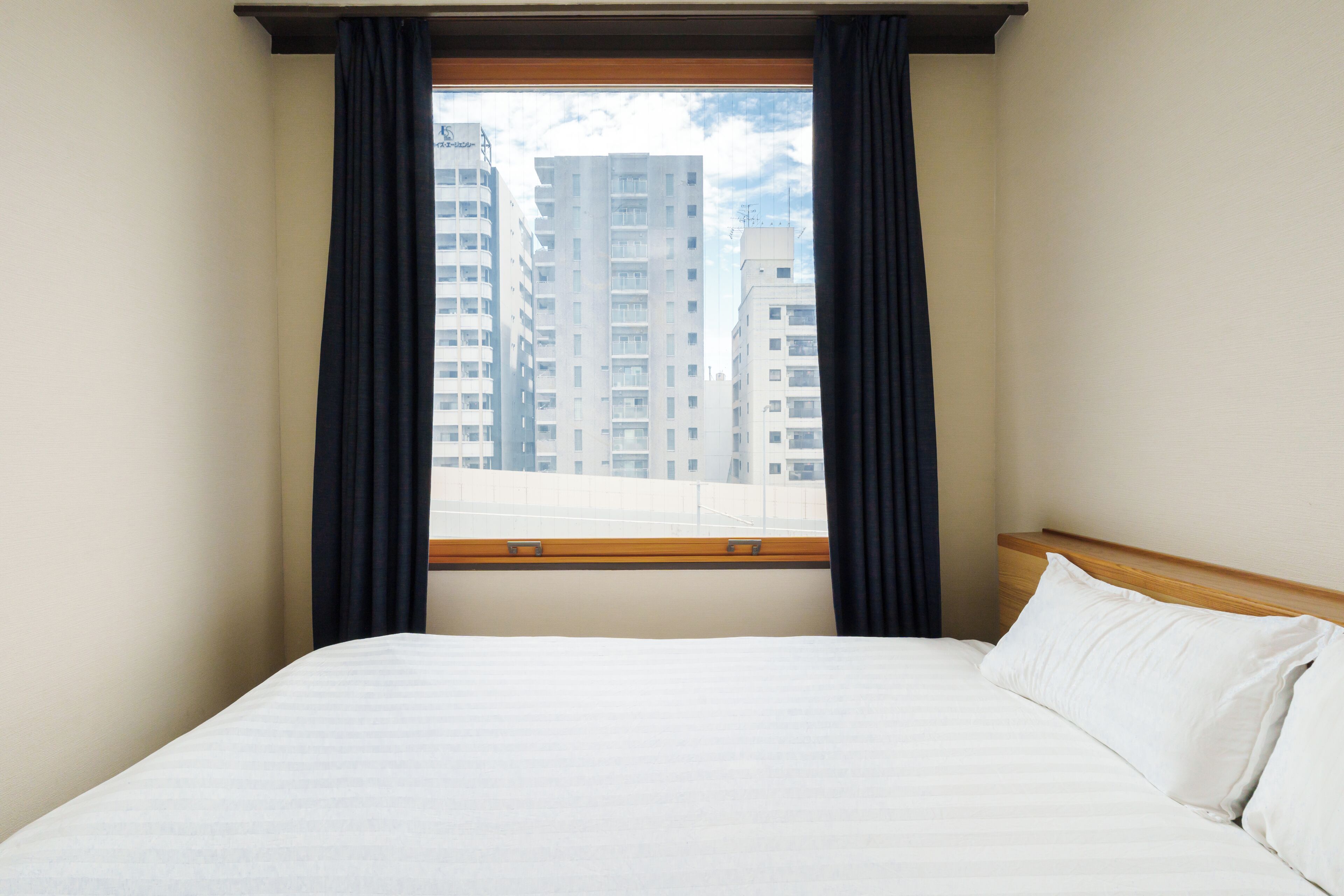 Habitació d'hotel amb un llit, una finestra amb cortines i vista a edificis alts.