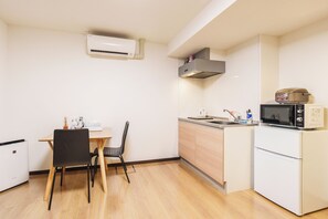 A compact kitchen with a microwave, a small sink, and a dining area with a table and chairs. - SERENE Osaka | 2 Minutes from Nipponbashi Station | 6F-606 | 35 ㎡, 2BR (osaka)