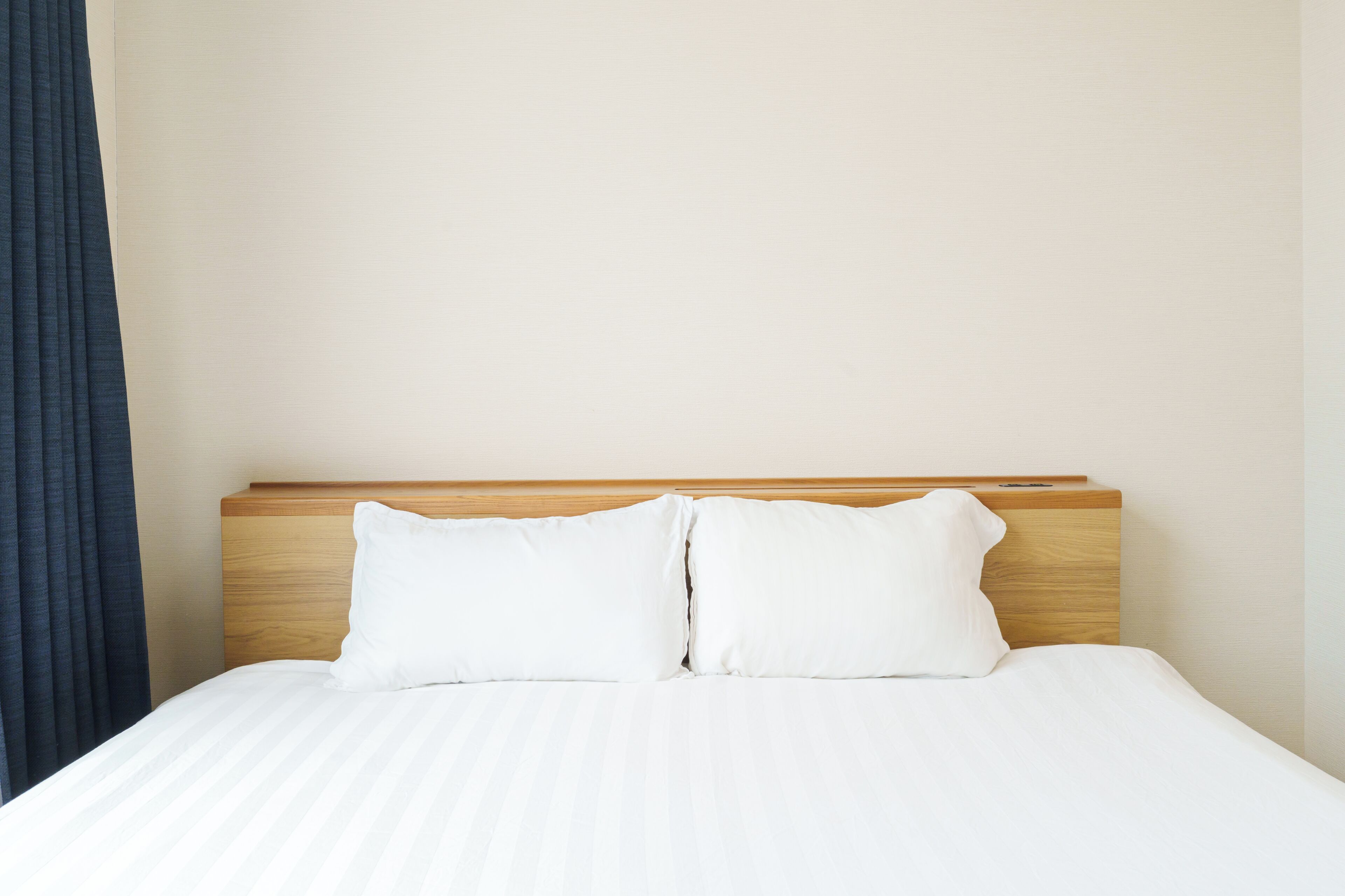 Una cama con cabecera de madera, ropa de cama blanca y una pared lisa.