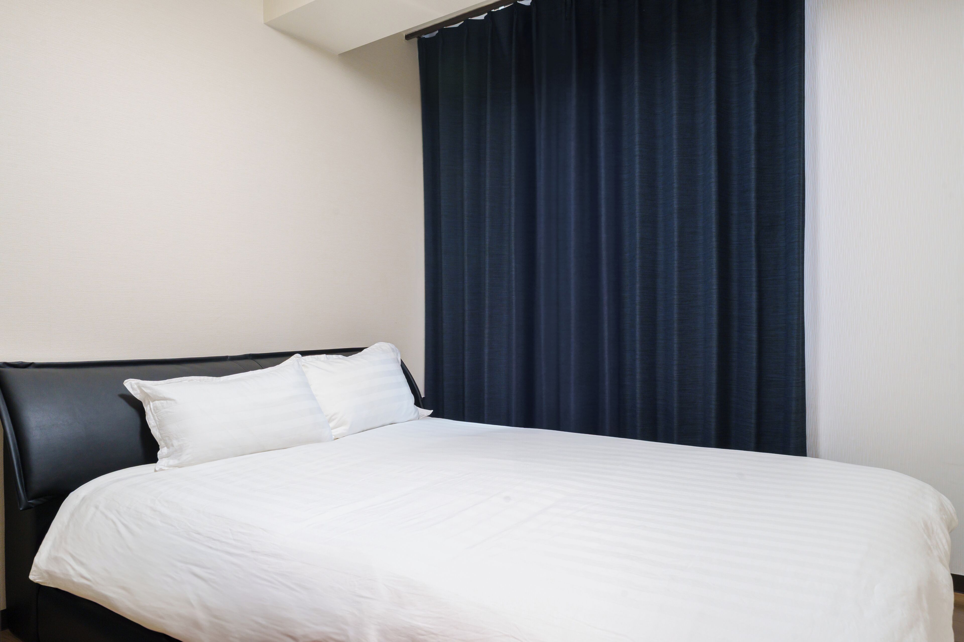 A hotel room with a bed, a dark curtain, and a white wall.