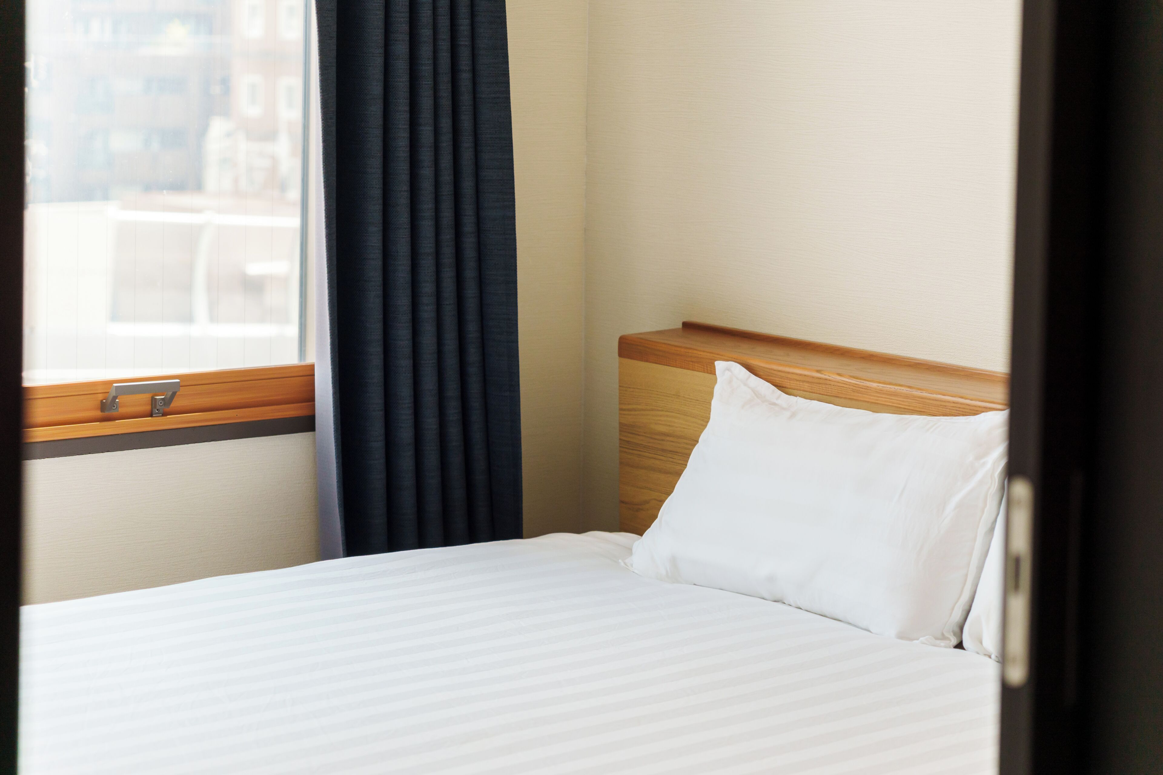Une chambre d’hôtel avec un lit, une fenêtre avec des rideaux et une vue sur les bâtiments environnants.