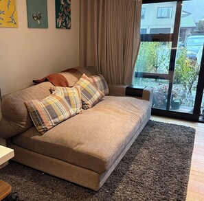 A modern living room with a sofa, a rug, and a window with a view of a building and trees.