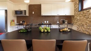 Une cuisine moderne dotée d’un îlot central, de meubles blancs, d’un mur de crédence en briques et d’un mur d’accent en pierre.