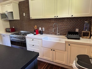 A kitchen with white cabinets, a brick backsplash, a stainless steel stove, and a black countertop.