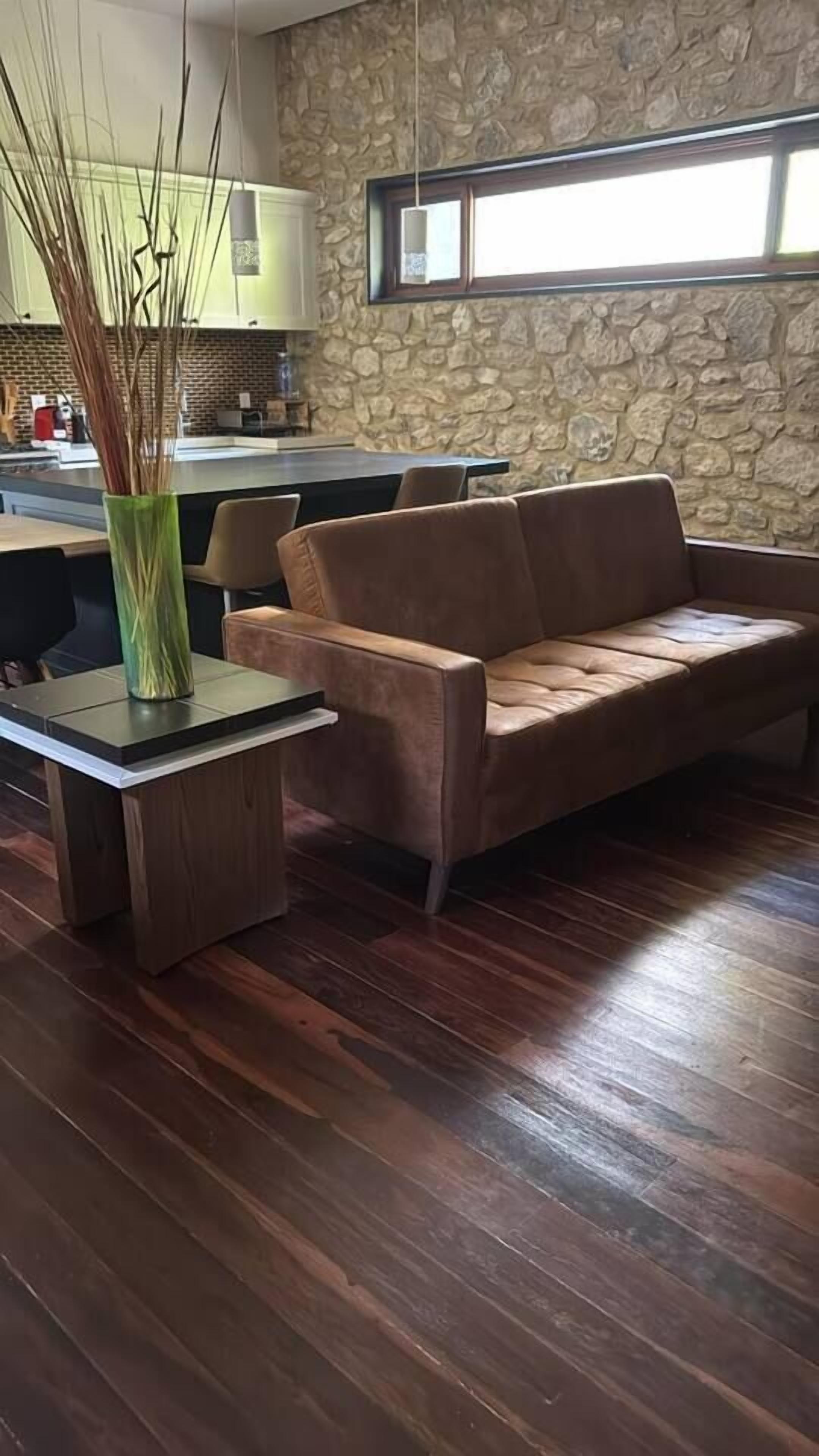 Une pièce avec un mur en pierre, un canapé en cuir marron, une table basse en bois et un vase décoré de branches.