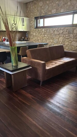 A room with a stone wall, a brown leather sofa, a wooden coffee table, and a vase with branches.