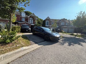 A residential street with houses, a driveway, and parked cars.
