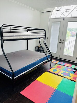 Una cama litera con colchón, una mesita con lámpara y una alfombra de juegos colorida en el suelo.