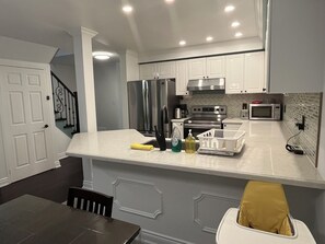 A modern kitchen with white cabinets, stainless steel appliances, and a marble countertop.
