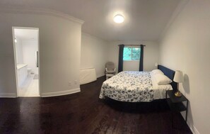 A bedroom with a bed, a nightstand, a window with curtains, and a door leading to a bathroom.