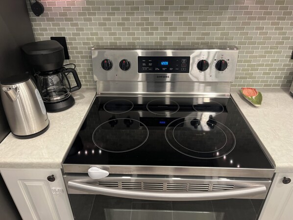 A stainless steel Samsung electric stove with four burners, a digital clock, and a control panel with various settings.