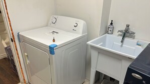 Et lille vaskerum med vaskemaskine, håndvask og en mindre opbevaringskasse.