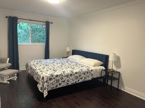 A bedroom with a bed, a nightstand, a chair, and a window with curtains. - Ravine Villa 4bed 4 bath fully privet (Richmond Hill)