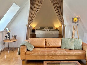A bedroom with a bed, a standing lamp, a tripod with a light, and a small table with a bucket.