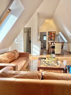 A spacious loft with a high ceiling, a leather sofa, a dining area with wicker furniture, and a painting on the wall. - Holiday apartment in heart of Møn (Stege)