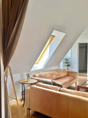A loft-style room with a sloped ceiling, a beige leather sofa, a small round table, and a skylight. - Holiday apartment in heart of Møn (Stege)