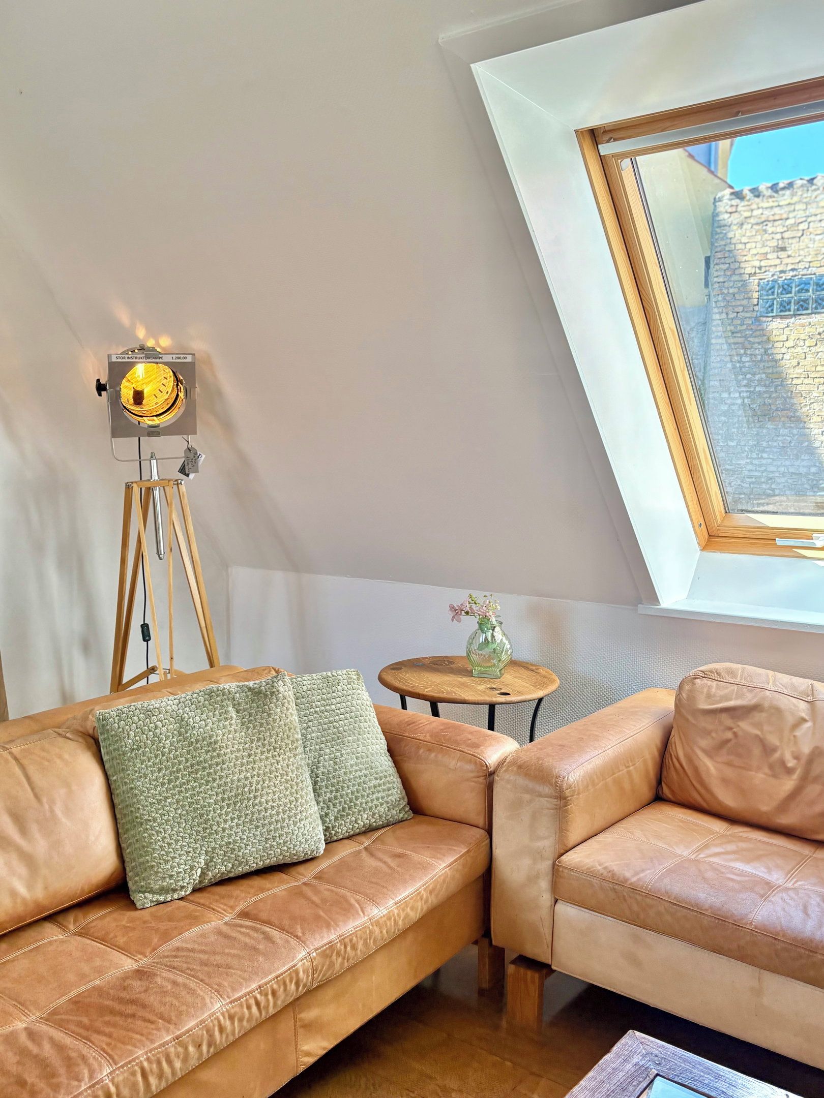Een slaapkamer in loftstijl met een schuine plafond, een telescoop, een klein rond tafeltje met een vaas, en een leren bank.