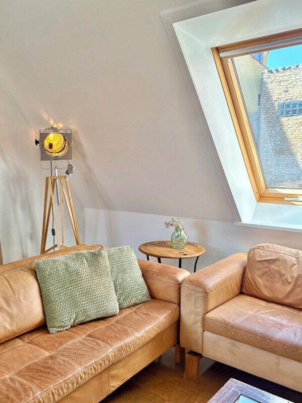 A loft bedroom with a sloped ceiling, a telescope, a small round table with a vase, and a leather sofa.
