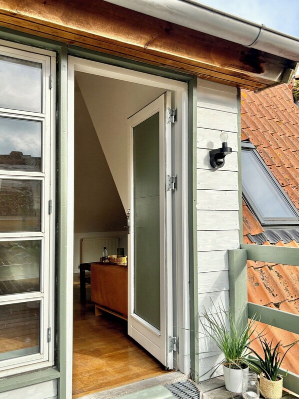 A residential property with a sliding glass door leading to an interior space, a small outdoor seating area with a table and chairs, and a potted plant on the porch.