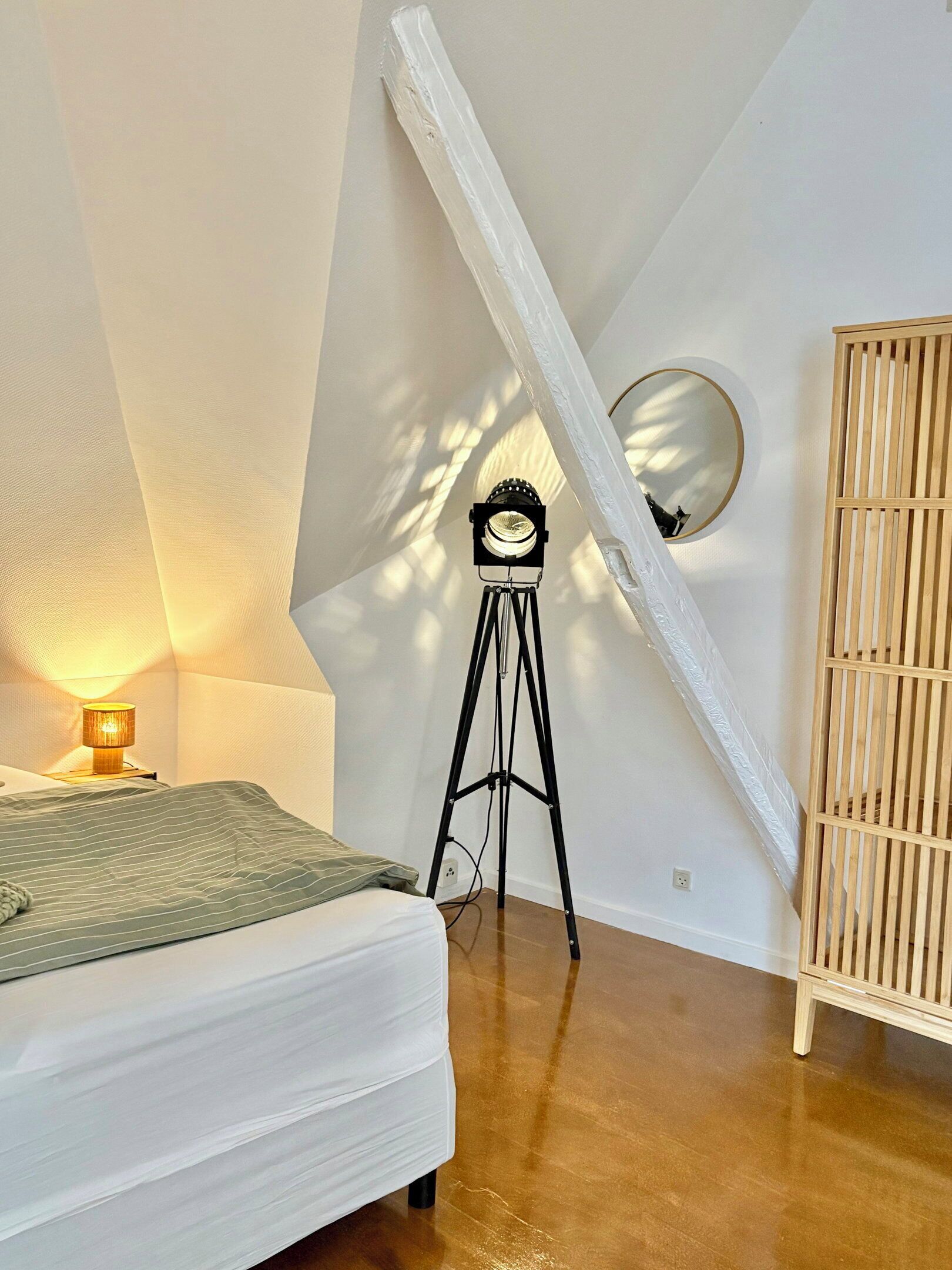Et soveværelse med en seng, en lampe, et stativ med et ur og et træskab.