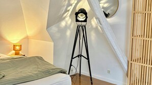 Ett sovrum med en säng, en lampa, ett stativ med en klocka och ett träskåp.