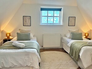 A bedroom with two beds, a window, a radiator, and wall art.