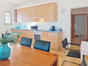 Uma cozinha moderna com armários de madeira, uma mesa de jantar com cadeiras, uma cafeteira e um rádio.