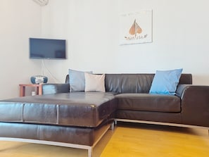 Un salon moderne avec un canapé d’angle, un téléviseur à écran plat et une petite table sur laquelle est posée une enceinte.