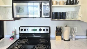 A kitchen with a stove, a microwave, and a set of knives on the counter. - Downtown Loft w/ Pool, Gym & Parking - Walk to Sundance Square (Fort Worth)