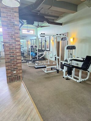 Ein Fitnessraum mit Trainingsgeräten, einer Ziegelstütze und einem Deckenventilator.