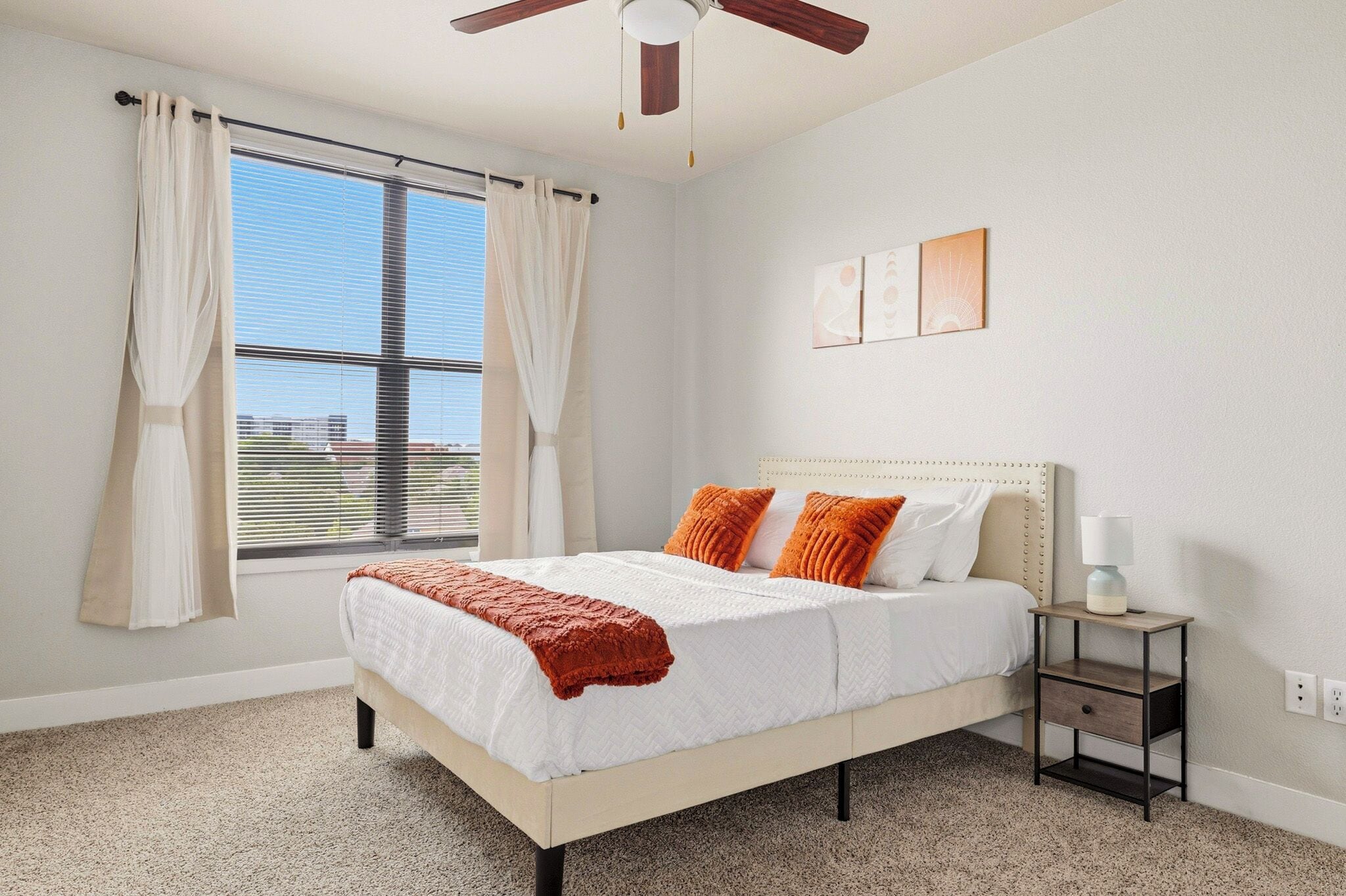A bedroom with a bed, a nightstand, a ceiling fan, and a window with curtains.