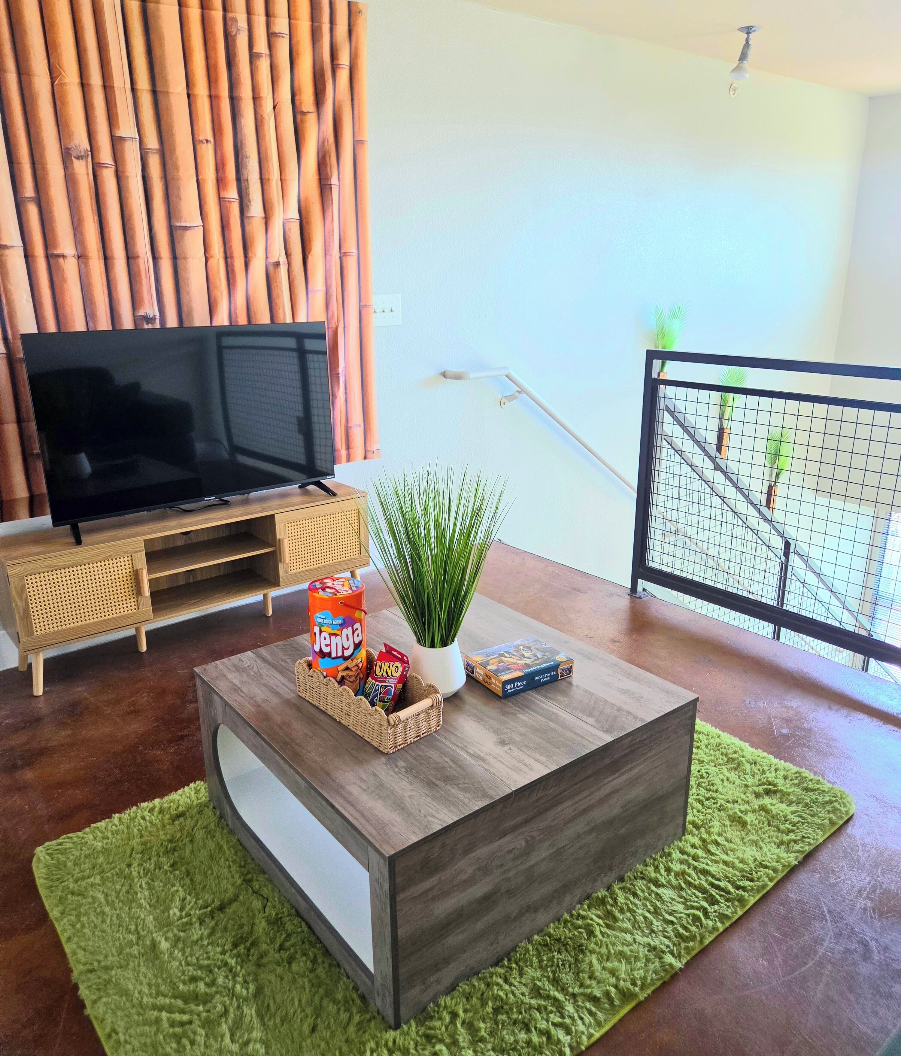 Una sala de estar con televisor, una mesa de centro con aperitivos, una planta y vistas a un balcón.