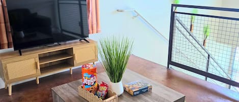 Un salon avec une télévision, une table basse avec des collations, une plante et une vue sur un balcon.