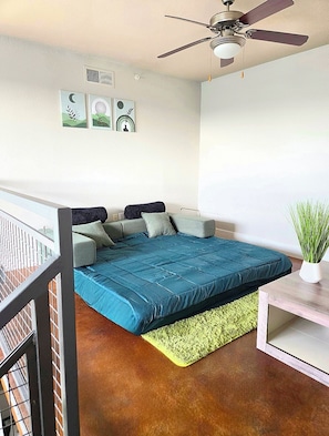 Ein Schlafzimmer mit einem Bett, einem Deckenventilator, einem grünen Teppich und einer Topfpflanze.