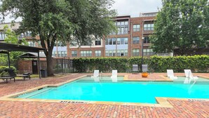 A swimming pool with a brick patio, lounge chairs, and a building in the background. - Downtown Loft w/ Pool, Gym & Parking - Walk to Sundance Square (Fort Worth)