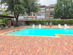 Ein Pool mit Pflasterterrasse, Liegestühlen und einem Gebäude im Hintergrund.