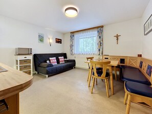 Ein Wohnzimmer mit einer Couch, einem Esstisch mit Stühlen, einem Fernseher und einem Kruzifix an der Wand.