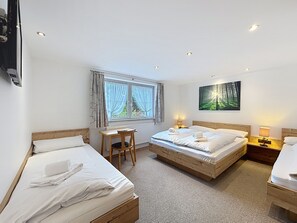 Une chambre d’hôtel avec deux lits simples, un bureau, une chaise, un radiateur et un tableau représentant une forêt.