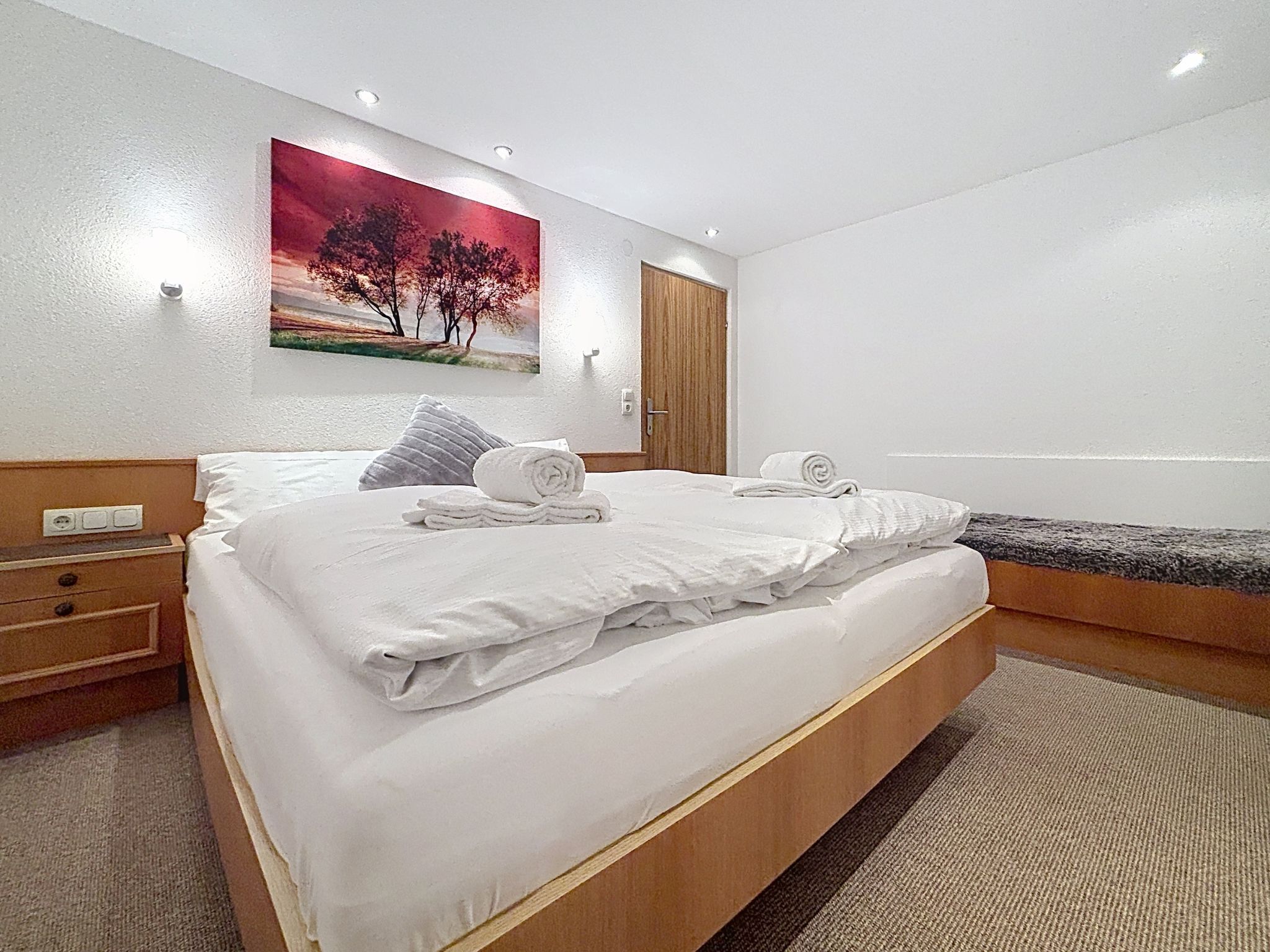 Quarto de hotel com cama, um banco, um quadro e uma porta.