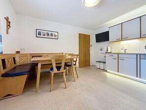 Ein Zimmer mit einem Holzespeisetisch und Stühlen, einer kleinen Küchenzeile mit Schränken und einem Fernseher, sowie einer Tür.