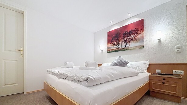 Habitació d'hotel amb un llit, una tauleta de nit, una làmpada penjada a la paret i un quadre.