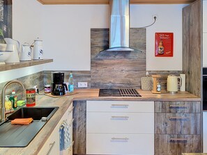Une cuisine moderne équipée d’une cuisinière intégrée, d’une machine à café et d’une bouilloire posées sur le plan de travail.